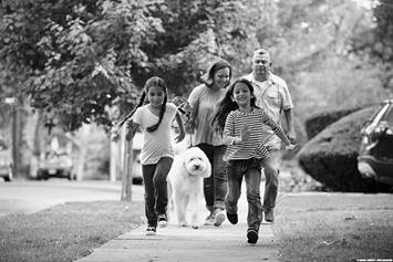 Family of four running with their dog on the sidewalk