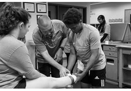 A workshop participant is wrapping a woman's ankle. The athletic trainer is watching and providing active instruction.