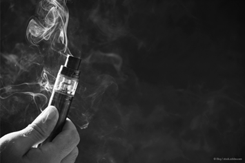 A hand holds an electronic cigarette emitting visible vapor against a dark background.